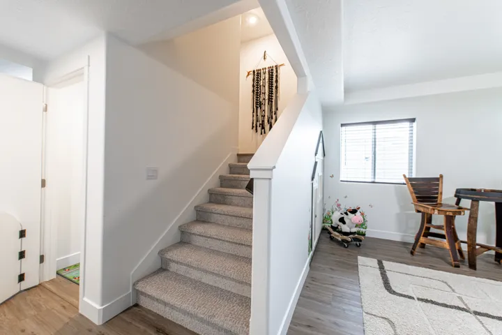 Carpeted staircase with white balustrade, wood-finish flooring, white walls, and a window with blinds
