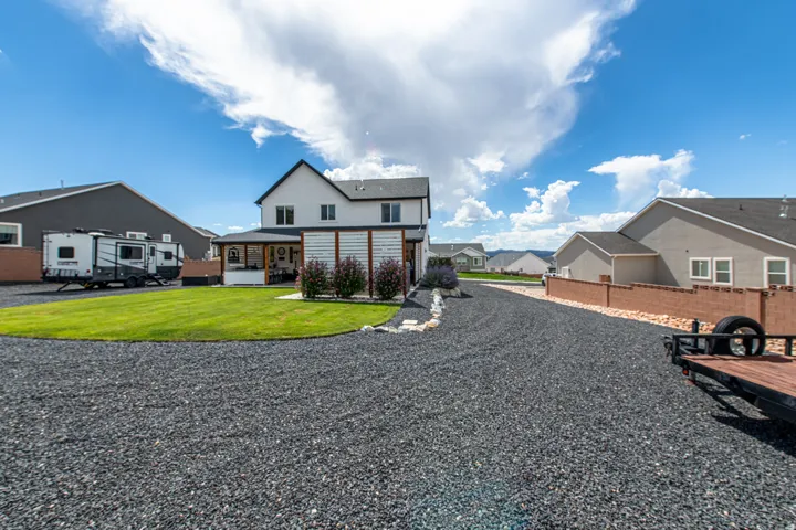 Expansive gravel driveway, manicured lawn, and a covered outdoor patio