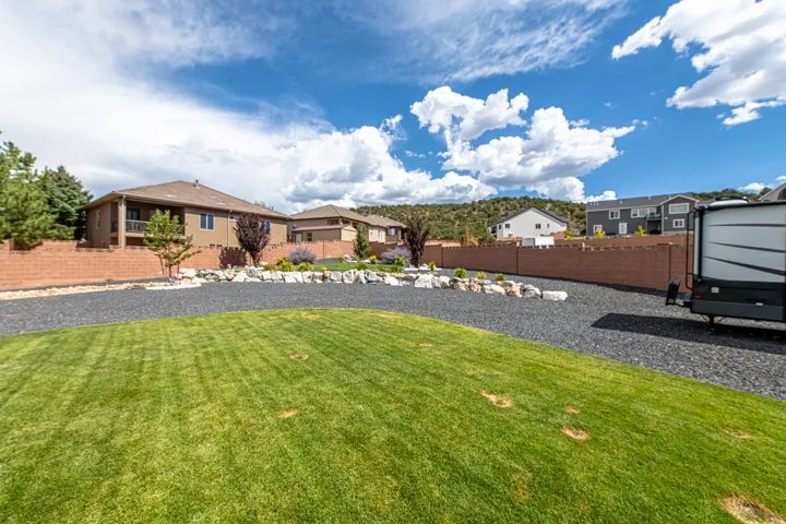 Expansive outdoor area featuring a manicured lawn, a gravel drive, and a retaining wall