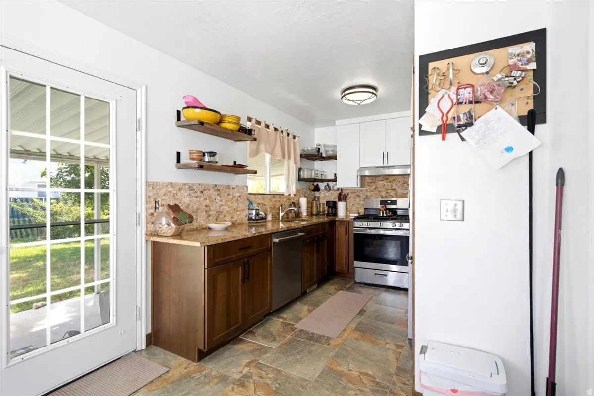 Kitchen featuring brown base cabinetry, white upper cabinetry, stainless steel appliances, and an intricate tile backsplash
