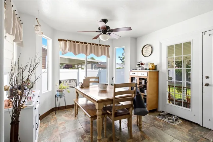Bay window dining area with multiple windows, ceiling fan, and stone-look flooring