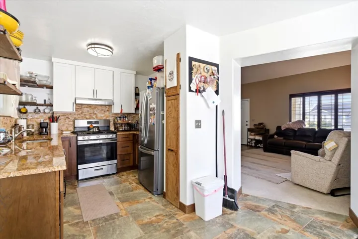 Kitchen featuring stone tile flooring, stainless steel appliances, upper white cabinetry, lower wood cabinetry, and a stone backsplash