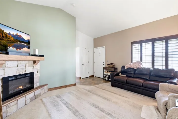 Vaulted ceiling, stone-clad fireplace with mantel, built-in electric fireplace insert, and window with plantation shutters