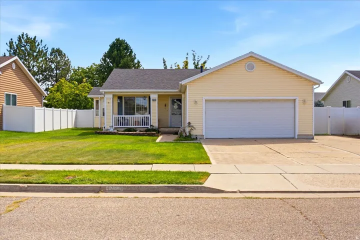 Yellow siding exterior with white trim, covered front porch, attached garage, concrete driveway, and white privacy fencing