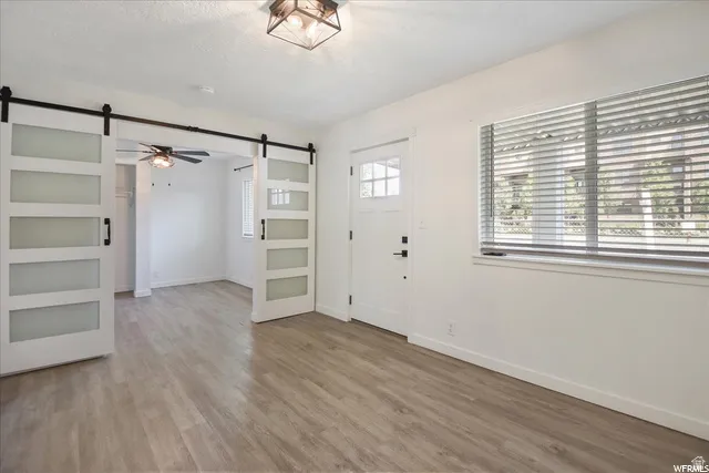 Wood-finish flooring throughout, white interior door with decorative lite, white window blinds, and white barn doors with frosted panels