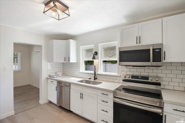 White shaker cabinetry with black hardware, stainless steel appliances, light-toned countertops, subway tile backsplash, and wood-finish flooring