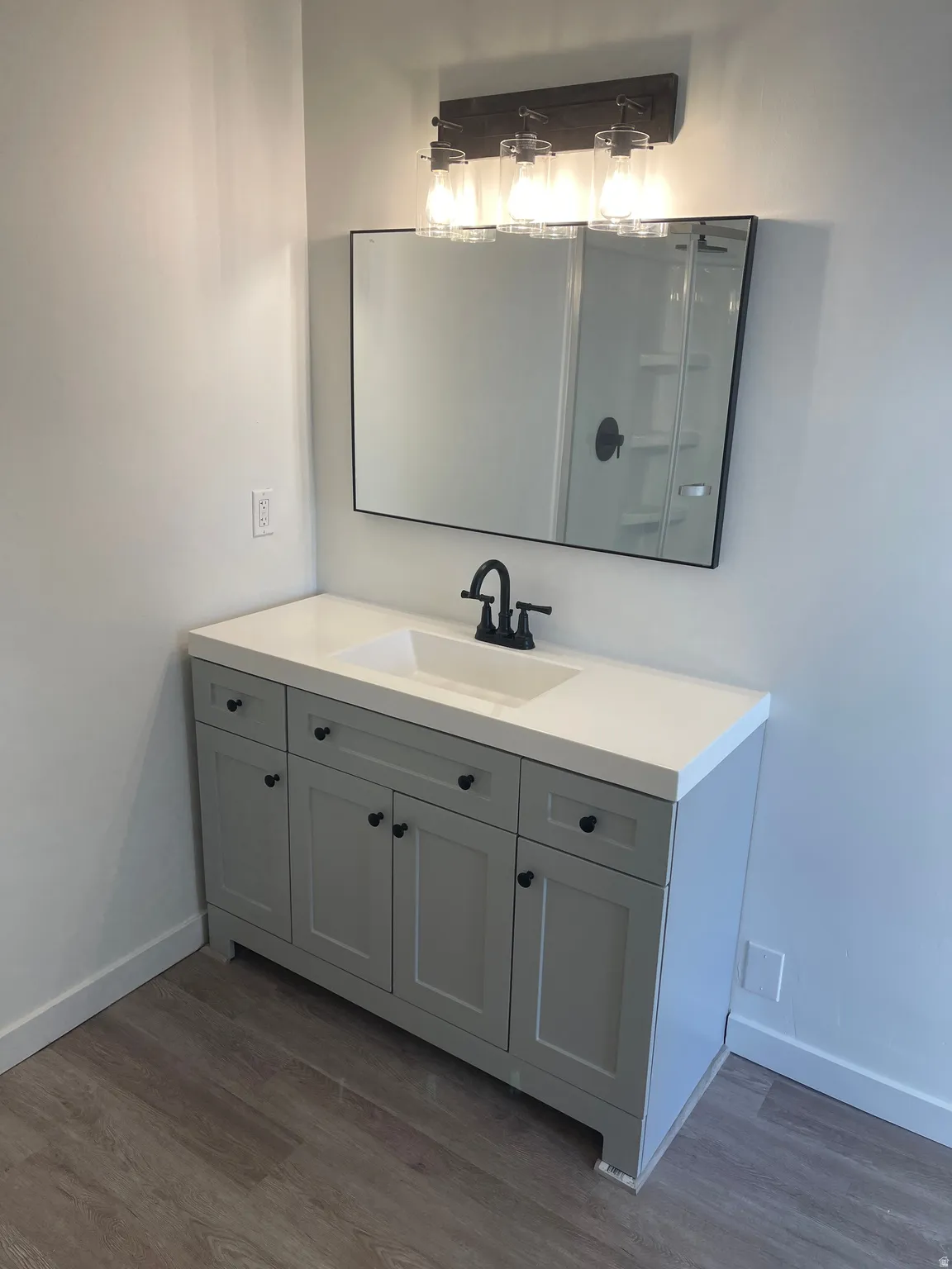 Vanity with shaker-style cabinetry, matte black hardware, integrated sink, and wood-finish flooring