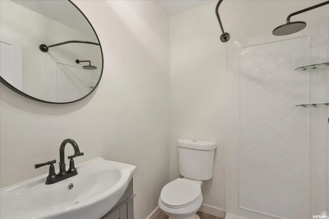 Modern bathroom featuring a circular mirror, dark bronze fixtures, a white ceramic sink, and a shower with a patterned surround and glass shelving