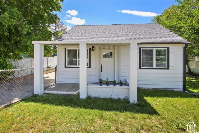 White siding exterior, covered front porch, dark-trimmed windows, gray shingle roof, and a chain-link fence