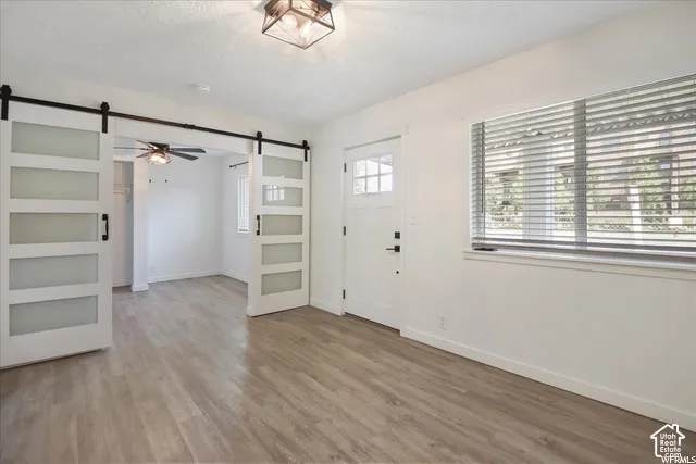 Wood-finish flooring throughout, white interior door with decorative lite, white window blinds, and white barn doors with frosted panels