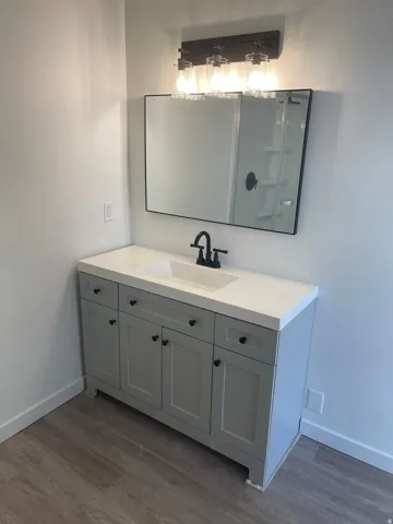 Vanity with shaker-style cabinetry, matte black hardware, integrated sink, and wood-finish flooring