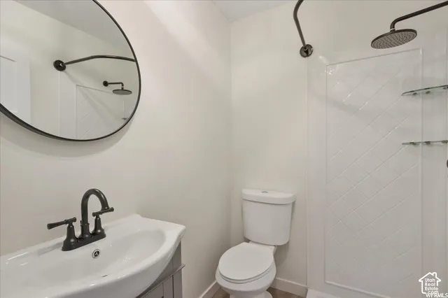 Modern bathroom featuring a circular mirror, dark bronze fixtures, a white ceramic sink, and a shower with a patterned surround and glass shelving