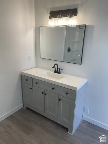 Vanity with shaker-style cabinetry, matte black hardware, integrated sink, and wood-finish flooring