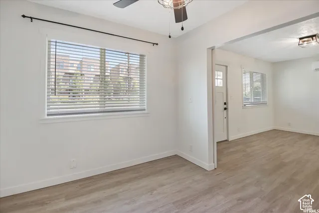Neutral interior featuring wood-finish flooring, ceiling fan with light fixture, white walls, and windows with horizontal blinds