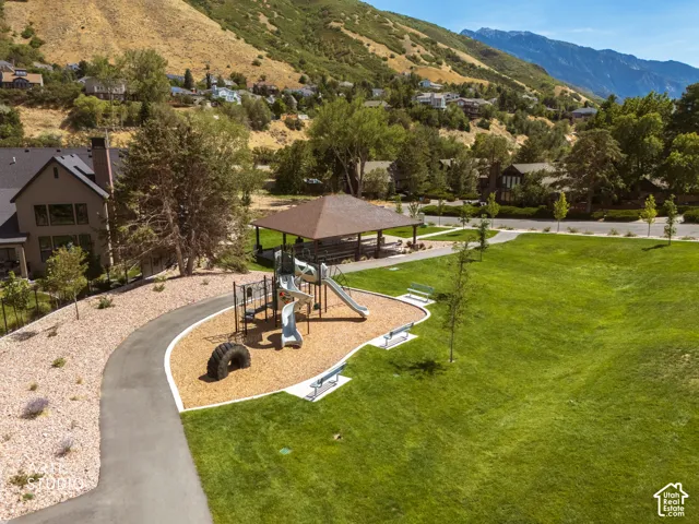 Expansive green space featuring a playground, covered picnic area, paved walking path, and mature trees