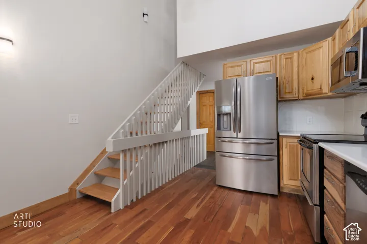 Hardwood flooring throughout, stainless steel refrigerator, stainless steel range, wood cabinetry, and a partial staircase with wood treads