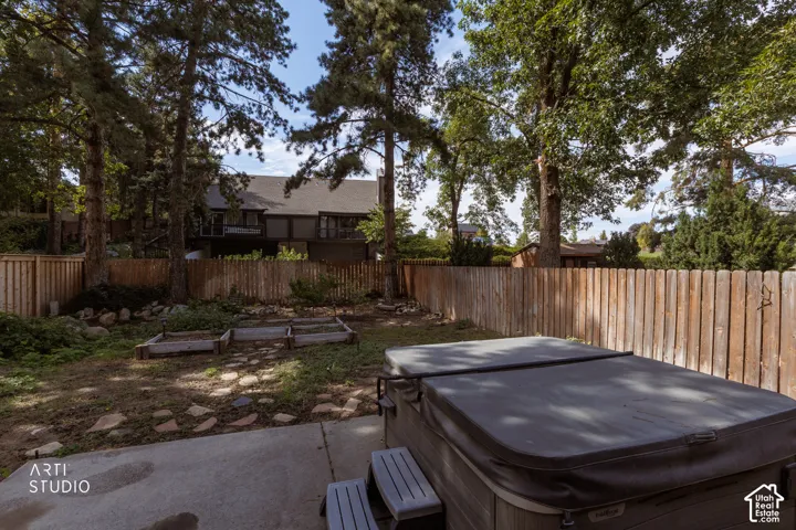 Backyard featuring a concrete patio, wooden privacy fence, mature trees, and raised garden beds