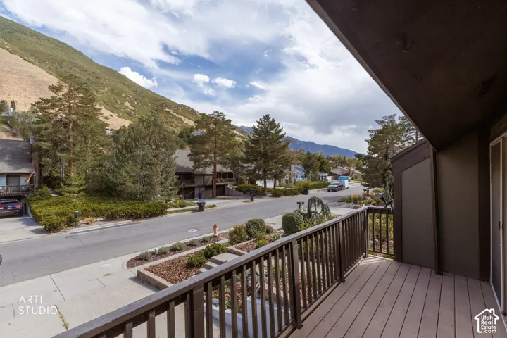 Balcony with composite decking and wood railing, offering a mountain backdrop and street scenery with mature trees and landscaped planting beds