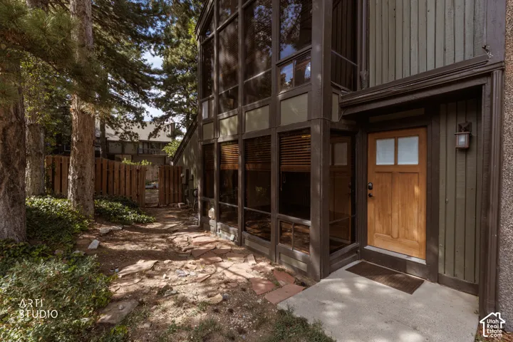 Wood-paneled entry door, vertical siding exterior, multi-pane windows, privacy fence, and concrete entry pad