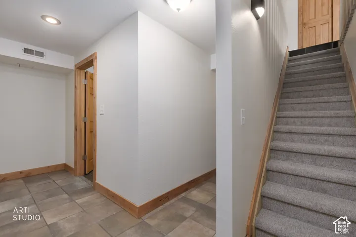 Tiled flooring, recessed ceiling lighting, light wood trim, carpeted stairs, and wall-mounted lighting