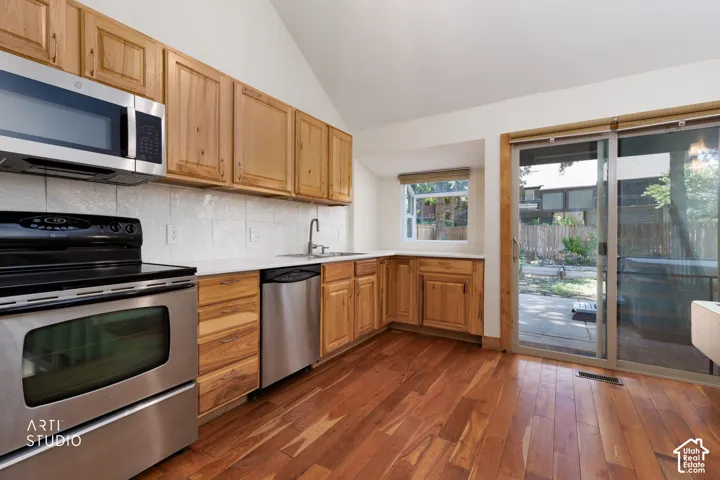 Wood-finish flooring, stainless steel appliances, light wood cabinetry, white countertops, and a full-light sliding door