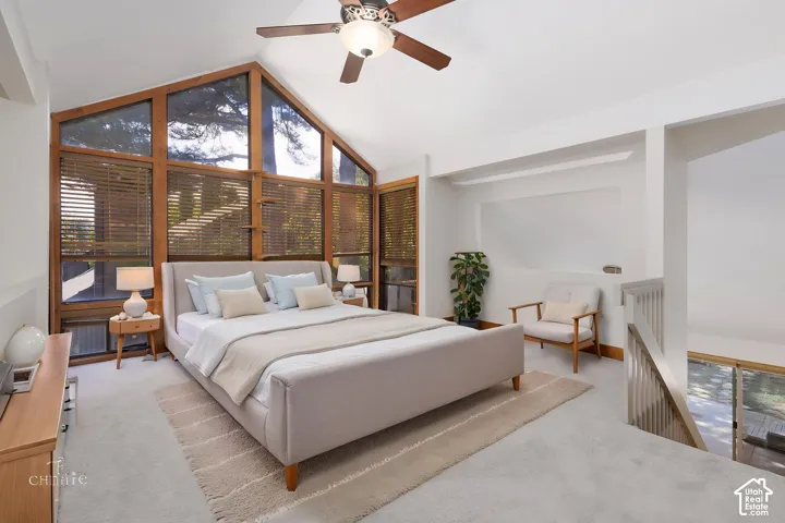Vaulted ceiling with a wood-finish ceiling fan, expansive wood-framed windows, light gray carpeting, and a white painted railing