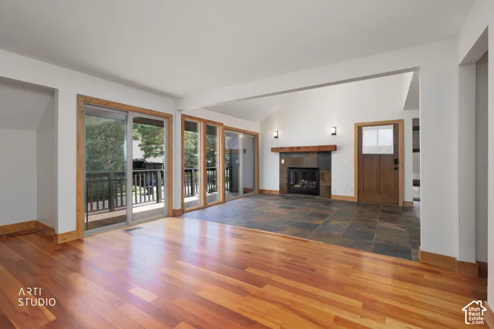 Vaulted ceilings, wood-finish flooring, multiple sliding glass doors, stone fireplace with wood mantel, and large format tile flooring