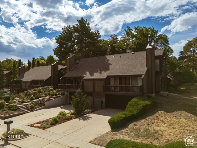 Sloped lot with tiered landscaping, multiple balconies, attached garage, and mature trees