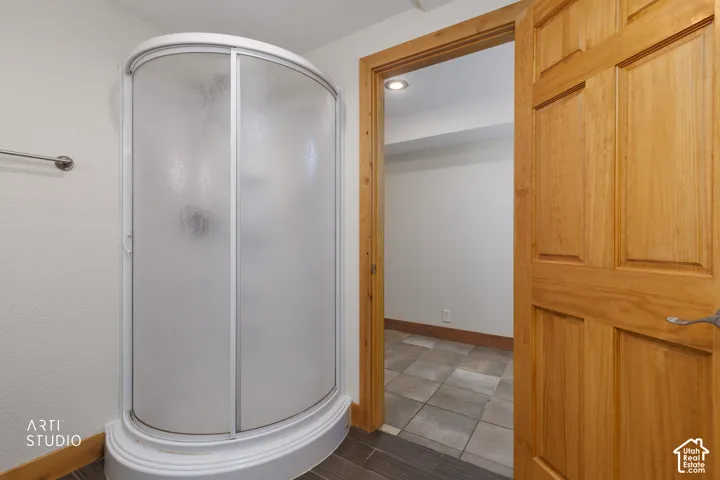 Curved shower enclosure with frosted glass, wood panel door, and tile flooring