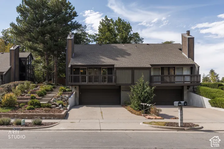 Terraced landscaping with mature plantings, multiple balconies, two garage doors, and a shingled roof