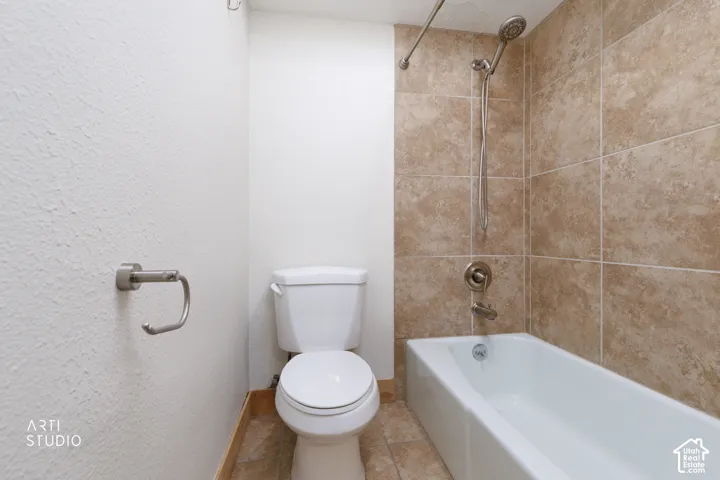 White bathtub with a built-in shower featuring a handheld showerhead and full-height tiled surround