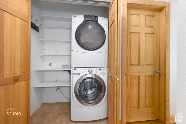 Full-size stacked laundry appliances, adjustable white shelving, light wood-finish paneled door, and neutral-toned flooring