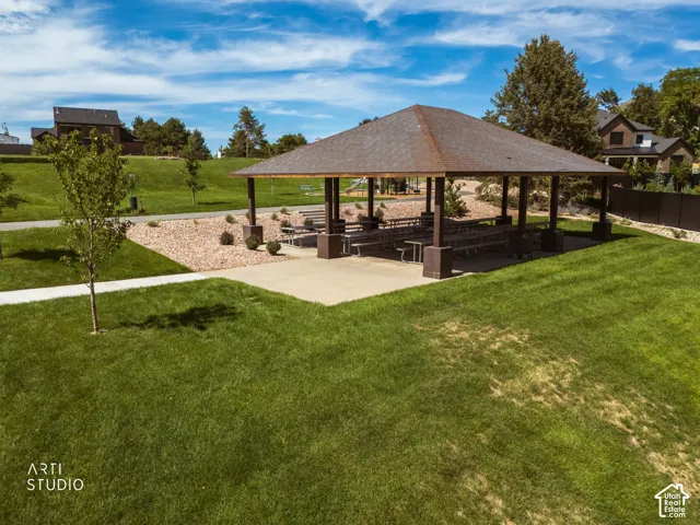 Expansive green lawn with a paved walking path, leading to a covered pavilion with multiple picnic tables and a concrete pad