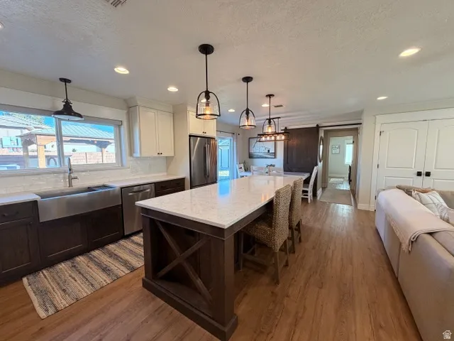 Spacious kitchen featuring a large island with seating, stainless steel appliances, a farmhouse sink, and wood-finish flooring