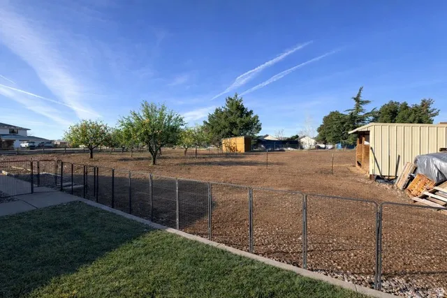 Expansive outdoor area featuring mature trees, a metal storage structure, a perimeter fence, and a paved walkway