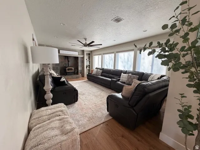 Spacious interior featuring wood-finish flooring, recessed lighting, and a prominent stone-clad fireplace with a wood-burning stove