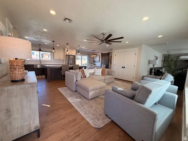 Recessed lighting, wood-finish flooring, two-tone kitchen cabinetry, kitchen island with seating, and a ceiling fan