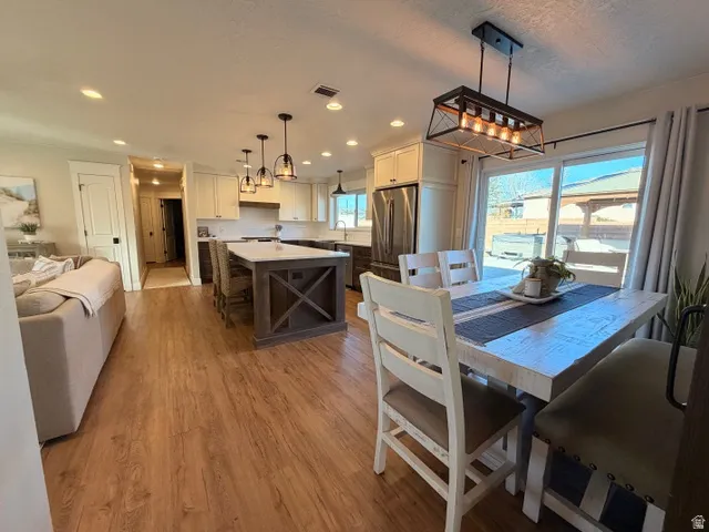 Wood-finish flooring throughout, kitchen with white upper cabinetry, large central island, stainless steel appliances, and recessed lighting