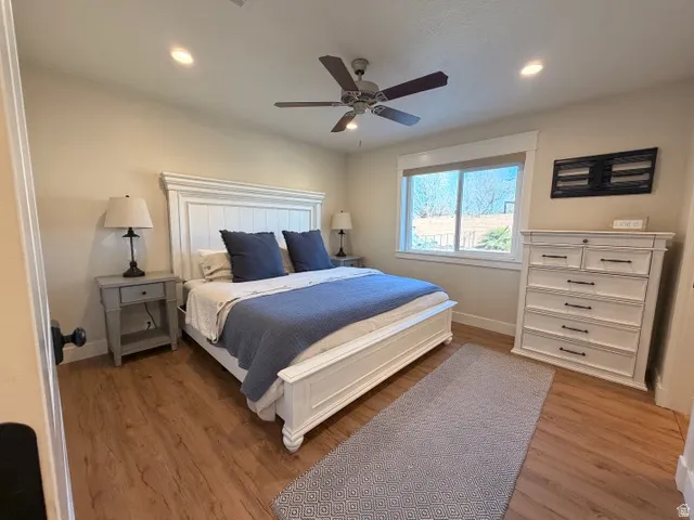 Recessed lighting, wood-finish flooring, a ceiling fan, and a window with a roller shade
