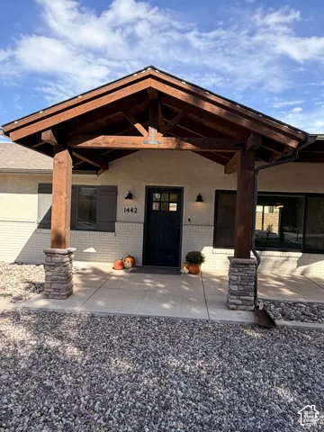 Covered entryway featuring timber-frame trusses, stone-base columns, light-colored brick exterior, and a multi-pane glass entry door