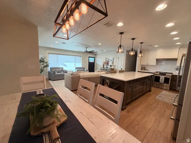 Kitchen with a large island featuring pendant lighting, stainless steel appliances, wood-finish flooring, and recessed lighting