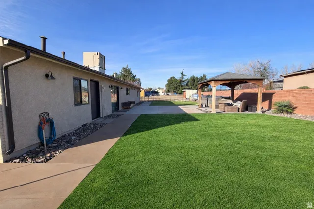 Expansive grass lawn with a paved pathway, leading to a built-in gazebo and an exterior wall with stucco finish