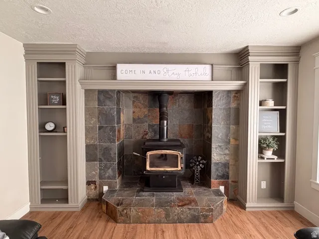 Wood-finish flooring, recessed lighting, built-in shelving, stone tile fireplace surround, and a wood-burning stove