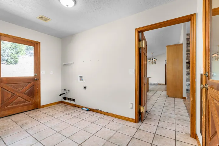 Tile flooring, wood-finish exterior door with glass insert, wood trim, and utility hookups