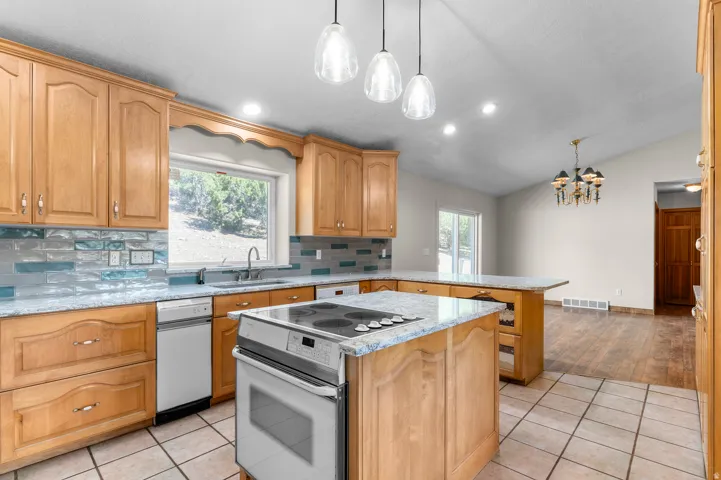 Kitchen featuring light wood cabinetry, a tiled backsplash, dual-level island, and tile flooring