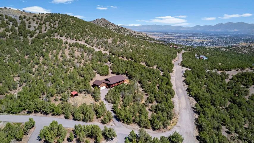 Expansive property featuring a brown multi-level residence, a private driveway, and a red shed structure, surrounded by abundant evergreen trees and mountainous terrain
