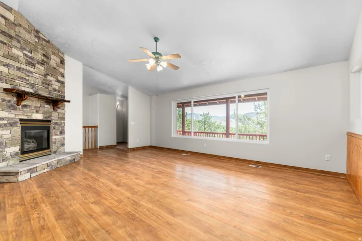 Spacious room featuring wood-finish flooring, a stone-clad fireplace, and a large window with distant scenery
