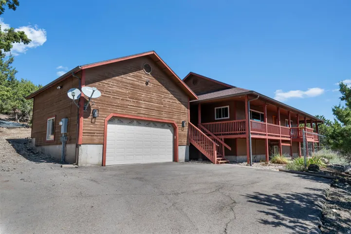 Rustic wood-sided residence featuring a two-car garage with white overhead doors, covered front porch with red railings, and multi-level deck structure