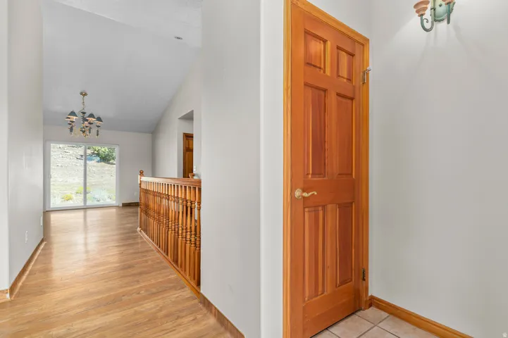 Vaulted ceiling, wood-finish flooring, built-in balustrade, sliding glass doors, and a decorative chandelier