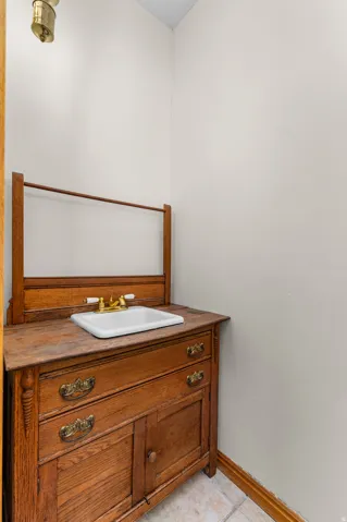 Wood vanity with integrated sink and brass-finish faucet, featuring carved wood details and decorative drawer pulls, set on light-toned tile flooring